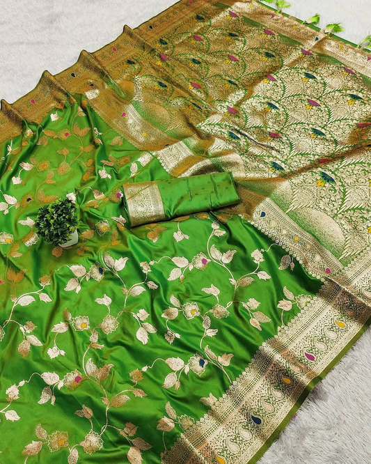 A green silk Banarasi saree with intricate gold zari floral embroidery and a wide gold border, displayed alongside a matching green blouse piece on a light gray textured surface.